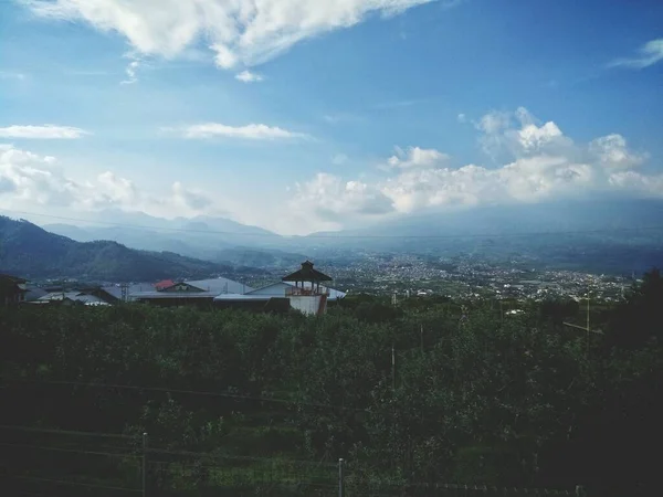 インドネシアの美しい高角度の朝の山の景色暗い雰囲気の中ではるかに混雑した住宅と明るい青空から見たバトゥ マラン市 — ストック写真