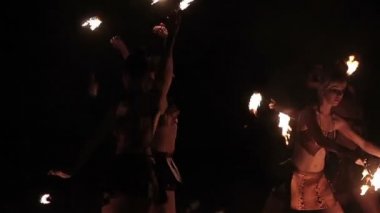 Fire show performance. Group of hot women female fire performers dance with burning fire torches on black background. Slow motion