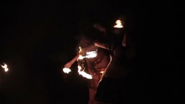 Fire show performance or dance competition. Group of sports women female fire performers dance gathering up burning fire torches and stand in final move on black background. Slow motion