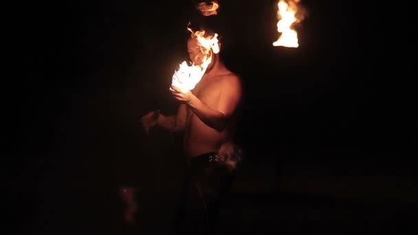 Пожарное шоу. Мужчина огненный исполнитель крутит горящую огненную веревку дротик пои на длинной веревке вокруг себя и делает огненное дыхание плюющимся пламенем на черном фоне. Медленное движение — стоковое видео