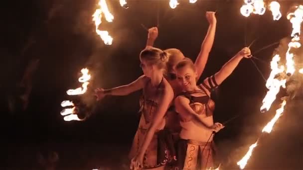 Spectacle de feu. Trois filles artistes féminines du feu se réunissent pour danser avec des torches de feu brûlantes en forme de ventilateurs sur fond noir. Gros plan. Mouvement lent — Video