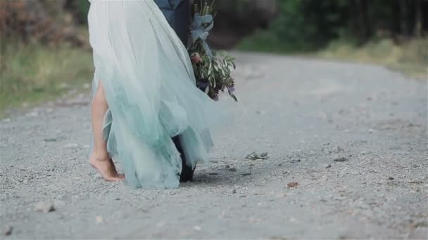 Les jambes féminines de la femme se tiennent sur la route avec l'homme la tenant pour baiser avec un bouquet de belles fleurs sauvages derrière son dos pour le cadeau surprise aucun visage méconnaissable sans visage. Gros plan — Video