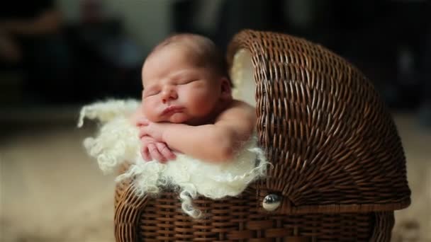 Pasgeboren schattige baby slapen met zijn hoofd rustend op zijn handen in een vintage rieten buggy of wieg binnenshuis de kamer — Stockvideo