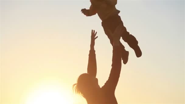 Felice giovane padre silhouette gettando piccolo figlio alto in aria in estate prato natura campagna parco al tramonto tempo retroilluminato rallentatore - ricongiungimento familiare felice infanzia giovane concetto di paternità — Video Stock