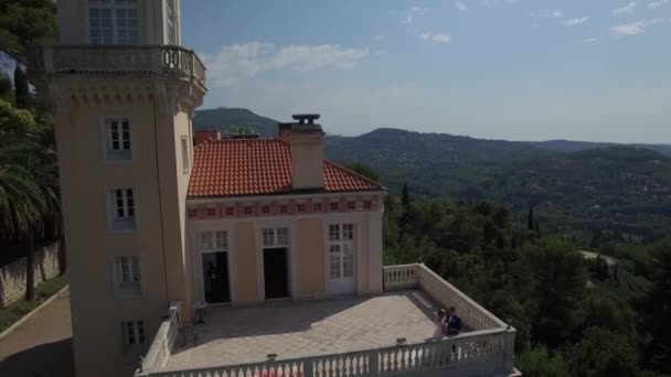 新婚的夫妇站在阳台上。新娘和新郎一起在阳台上的小欧洲法国格拉斯山地区的古代城堡。美丽的地方，结婚的一天。缩小无人驾驶直升机飞过 — 图库视频影像