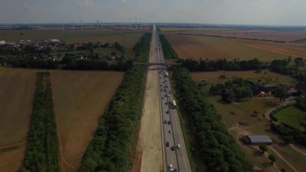 Pembangunan jalan raya multilane melebar di lapangan pedesaan dengan turbin angin dan jembatan lalu lintas jam sibuk mobil dan truk bergerak lambat Eropa Jerman 4K udara terbang dari atas — Stok Video