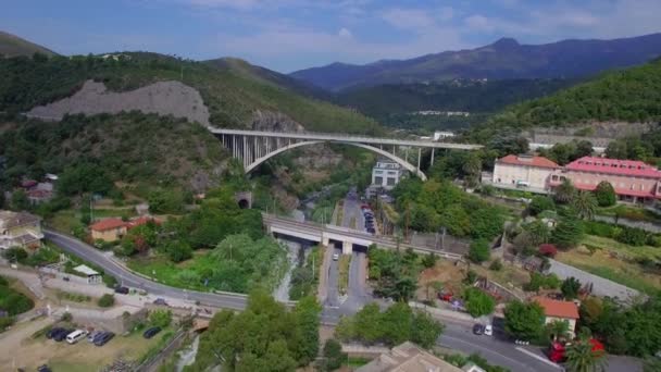 Puente de carretera en el túnel de montaña de roca hasta el puente ferroviario en la ciudad 4k avión no tripulado aéreo desde arriba. Vuele sobre los coches y el autobús que se mueve en el puente del arco en el rock río arriba y tren ferroviario en Italia o Francia Europa — Vídeos de Stock