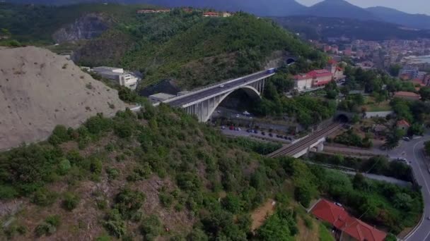 Transport traffic on mountain road and resort sea coastal town view 4k aerial drone from above. Fly over lorry trucks and cars move on overpass bridge interchange road junction Italy or France Europe — Stock Video