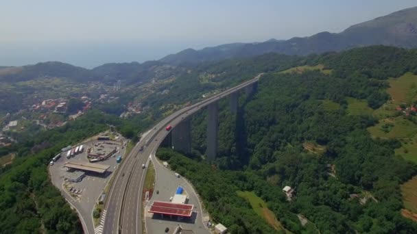 Bridge viaduct highway transport traffic aerial 4K. Fly over mountain overpass road with gas filling station and park lot for truck lorries cars moving in Italy Europe. Green hillside ecology top view — ストック動画