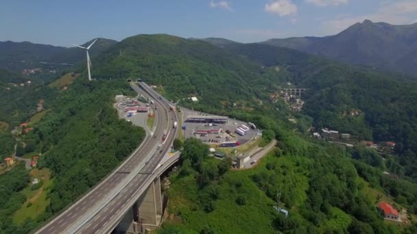 Highway mountain bridge viaduct road with gas filling station and park lots for truck lorries cars aerial 4k Europe Italy. Fly over rest charge green hillside wind turbine energy - top birds eye view — Stock Video