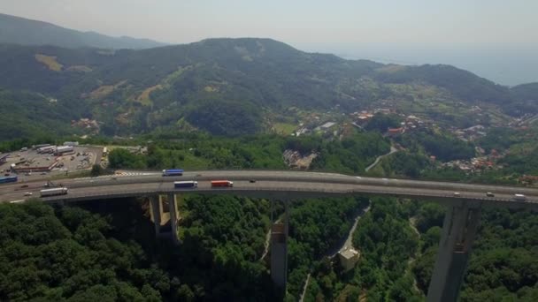 Bypass highway viaduct bridge above coastal sea town in Italy aerial 4k. Cars lorry truck cargo freight logistics. Vehicles move on massive bridge road above green valley top view from above by drone — ストック動画