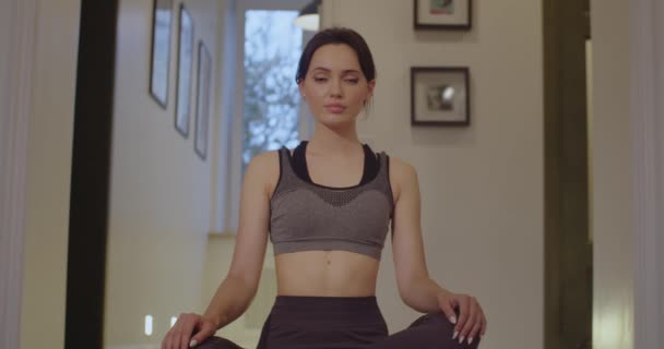 Indoors portrait of attractive girl practicing yoga at home slow motion natural light. Young woman sitting cross-legged doing seated twist stretch close up front view. Healthy lifestyle body care — Stock Video