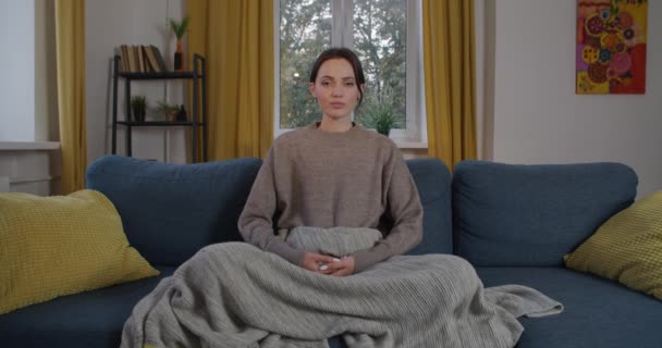 屋内でゆっくりとした動きで自宅で瞑想若い女性。忙しい1週間のスローモーションのリラックスしたホームソファに座って魅力的な女の子のフロントビュー。抗ストレス練習ライフスタイル — ストック動画