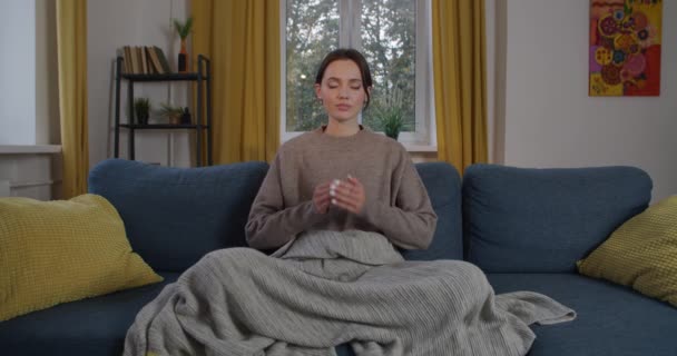 Vista frontal da senhora calma meditando em casa com palmas unidas em mudra Namaste. Mulher elegante sentado no sofá praticando relaxamento ioga após movimentado movimento lento workweek. Mindfulness estilo de vida espiritual — Vídeo de Stock