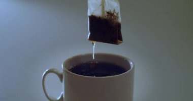 Siyah çay demleyen meçhul biri gri arka planda beyaz fincana çay poşeti koyuyor. Teabagging natural light slow motion fotokopi uzay metninin ön görüntüsünü kapat. Kafein sabah enerjisi 