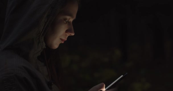 Porträt einer jungen attraktiven Frau nutzt Smartphone im Wald in Großaufnahme Schöne Brünette Mädchen Browsing auf Handy und Licht beleuchtet ihr Gesicht. Millennial Teenager scrollt durch ihr Handy — Stockvideo