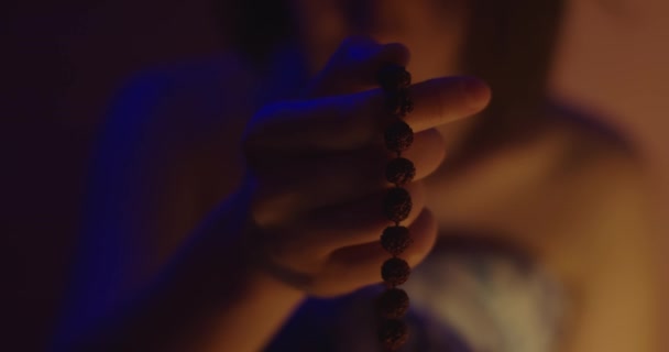 Macro dedos femininos dizendo budista rudraksha contas dentro de casa colorido luz da noite. Mulher branca rezando meditando em casa câmera lenta. Conceito de acessórios de prática espiritual oriental — Vídeo de Stock