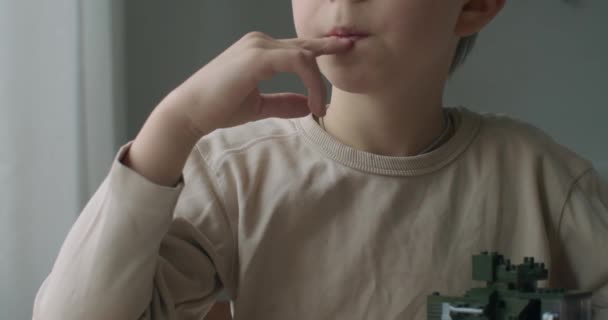 Close-up onderste helft gezicht portret van jongen zittend door het raam natuurlijk licht slow motion. Onherkenbaar kind spelen erector set lego binnen thuis. Macro lichaamsdelen handen lippen vingers creativiteit — Stockvideo