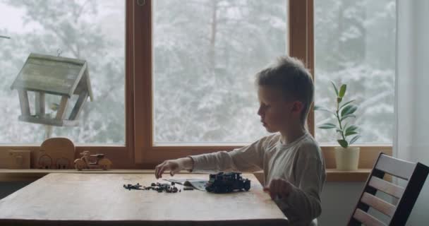 Кавказький хлопчик проводить час у відпустці, будуючи машину з цегли вдома. Бічний вид на дошкільнят, який грає з еректором, влаштовує іграшки у приміщенні за допомогою повільного віконного руху. Залишайся вдома. — стокове відео