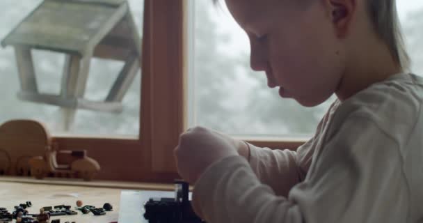 Extra närbild av pojke konstruera leksaker från tegel slow motion. Makro grunt porträtt av allvarliga barn leker med plast erektor inställd inomhus naturligt ljus. Barnaktiviteter — Stockvideo