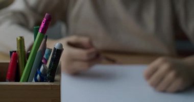 Renkli kalemlerin masa fotokopi uzay metninin üzerinde duran sığ görüntüsünü kapat. Kapalı alanda yavaş çekimde beyaz kağıda yazı yazan çocuk elleri. Eğitim geliştirme sanatı kavramı