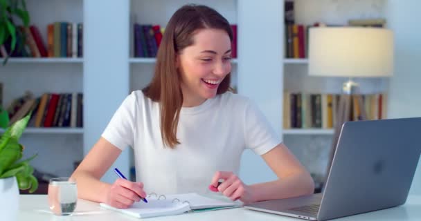 Mujer joven que estudia chat en línea a la cámara web de videollamada en coronavirus de bloqueo. Chica estudiante feliz sentado en la mesa de la PC hablando con el profesor haciendo notas en cámara lenta. Educación a distancia — Vídeo de stock