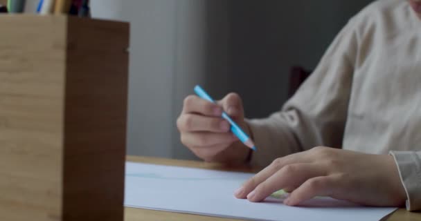 Dibujo infantil irreconocible con lápiz de color en papel en casa cámara lenta interior. Retrato detallado de mano del niño haciendo la tarea escolar solo en interiores. Concepto de educación primaria infantil — Vídeo de stock