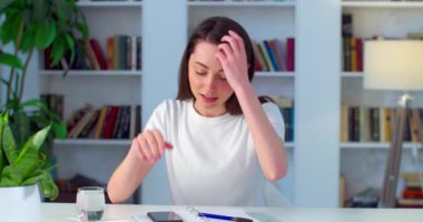 Cep telefonuyla ev içi iç mimari problemini çözen üzgün bir bayan öğrenci. Ciddi bir kadın akıllı telefonu elinde tutarak masada oturuyor ve yavaş çekimde çalışıyor. Duygular teknolojisi 