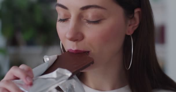 Foarte aproape de fetele senzuale se confruntă cu ciocolată dulce bar cu ochi închiși mișcare lentă. Macro portret detaliat al tinerei femei degustând desert de cacao în interior la domiciliu. Conceptul de protecție a dinților — Videoclip de stoc