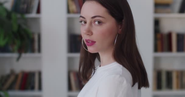 Side portrait of serious young woman looking to camera calmly indoors slow motion. Sensual sexy girl posing on bookshelf background. Solving problems life trouble. Female seduction self confidence — Stock Video