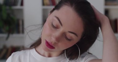 Genç şehvetli kız uzun saçlarını ayartır ve yavaş çekimde kameraya bakar. Beyaz kadın içeride poz veriyor doğal ışığı baştan çıkarmak için flört ediyor. Kadınsı güç kavramı 