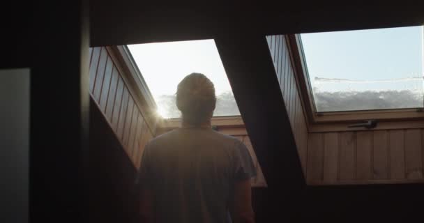 人室内のスローモーション上昇太陽を賞賛のバックビューのシルエット。青い空の自由を夢見て木製の窓の外を見て認識できない男。孤独孤独孤独の概念 — ストック動画