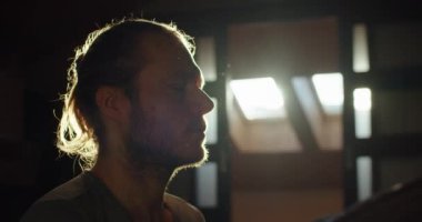 Sakallı bir adamın portresi. Yalnız meditasyon yapıyor. Sabah güneş ışınlarıyla yavaş çekimde. Yogi ustası ahşap evin iç dekorasyonuna kapalı gözlerle bakıyor. Huzur meditasyonu