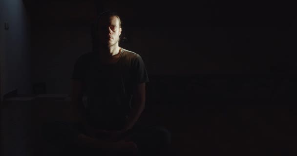 Portrait of man sitting in lotus asana meditating alone in dark room black background copy space. Pensive calm yogi practicing yoga meditation indoor morning light text. Tranquility calmness wellness — Stock Video