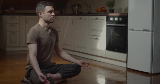 Langzame beweging van een serieuze jongeman die thuis mediteert in een gezellig appartement. Zijaanzicht van bebaarde persoon die yoga pranayama beoefent met gesloten ogen tijdens lockdown coronavirus. Ontspanning tegen stress — Stockvideo