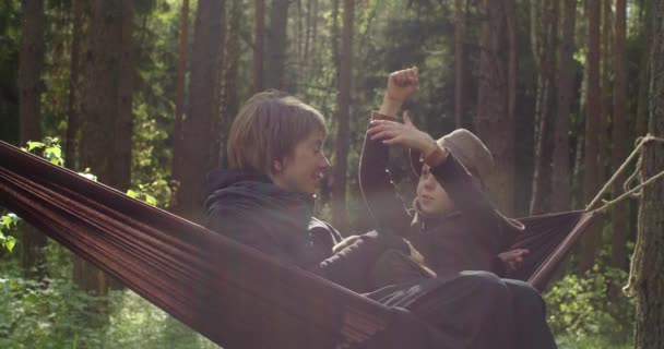 Happy couple mother kid relaxing in hammock in green coniferous forest slow motion. Two smiling people woman child having spending good time together natural sunshine. Close family relations — Vídeos de Stock