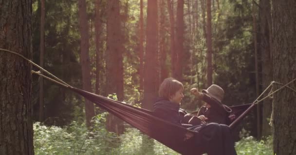 Happy family spending wonderful time together in golden sun rays outdoors. Relaxed woman and child swinging in hammock relaxing in wild forest park. Happiness freedom travel togetherness concept — Video Stock