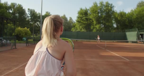 Strzał w zwolnionym tempie kobiety tenisistki ćwiczącej na korcie w letni słoneczny dzień. Dwie dziewczyny uderzające służąc piłkę spędzając wolny czas wstecz widok. Osiągnięcia sportowe aktywny styl życia — Wideo stockowe