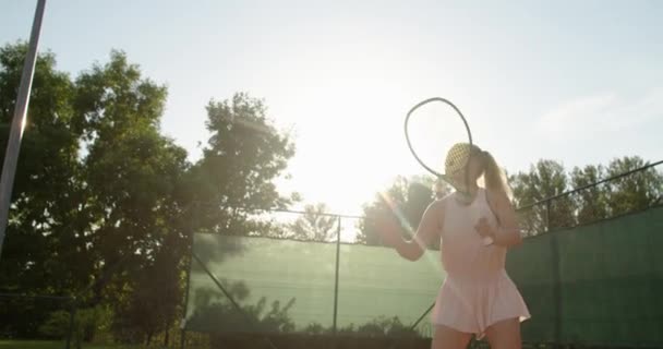 Slow-motion zijaanzicht van een jonge atleet traint het dienen van de tennisbal. Een tiener atleet speelt tennis op een veld. Een actief meisje slaat krachtig een bal tijdens het sporten — Stockvideo