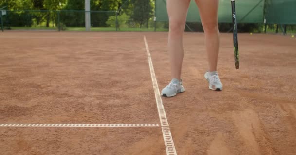 Låg vinkel ansiktslös idrottskvinna värmer upp innan tennismatch träffar bollen på lera domstol. Crop närbild av starka kvinnliga ben i sportkläder i sneakers tränare slow motion. Sportiv uniform — Stockvideo