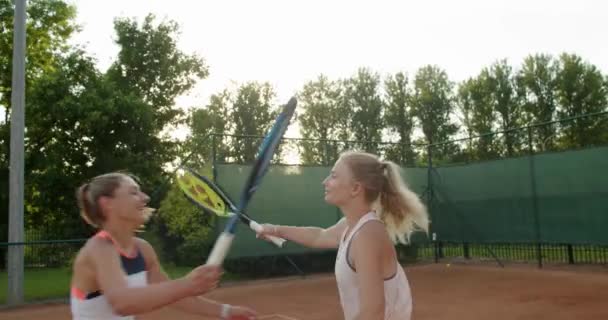 Dvě mladé atraktivní dívky objímající po tenisovém zápase venku na hliněném kurtu zpomalit. Profesionální ženské hráče objímající smích dokončovací hra. Přátelství sport zdravotní vztahy — Stock video