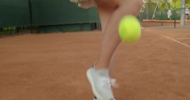 Νεαρή γυμνασμένη κοπέλα που σερβίρει την μπάλα σε αγώνα τένις πρωτάθλημα αργή κίνηση. Close up sliding view εφήβων αθλητών που ασκούν τον αθλητισμό σε πηλό δικαστήριο σε επαγγελματικό κιτ στολή. Αθλητικός ενεργός τρόπος ζωής — Αρχείο Βίντεο