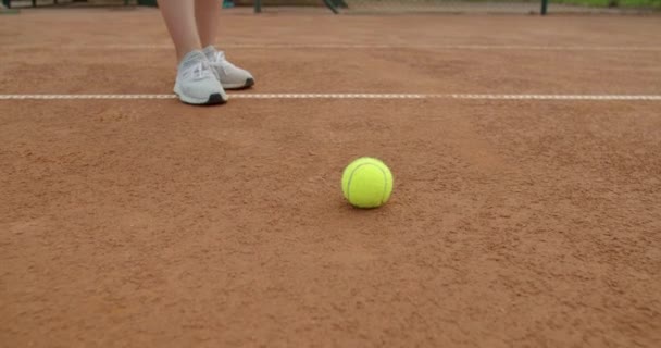 Nízký úhel pohledu na tenista skákající míč zvedající ho z jílového hřiště zpomaleného pohybu. Zblízka ženské ruce vyzvednout míč pro sportovní praxi venku. Příslušenství sportovního vybavení — Stock video