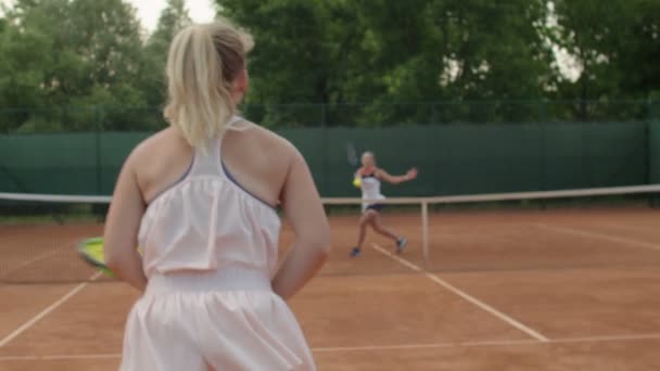 Açık hava kil kortunda tenis oynayan iki atletik kızın arka görüntüleri. Büyük kort iki profesyonel oyuncu bayanlar şampiyonluk için spor antrenmanı yapıyorlar. Spor giysileri aktif yaşam tarzı — Stok video