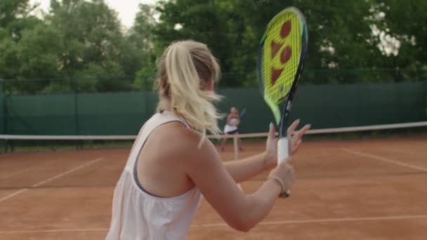 Professzionális sportos nő szolgálja tenisz labda ellenfél salakos pályán szabadban nyári háttér. Erős nők, akik aktív sportot űznek ütő lassított felvételekkel. állóképesség türelem koncepció — Stock videók