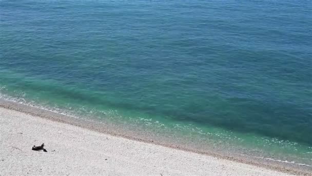 A person lying on a shingle beach and sunbathing near the ocean — Stock Video