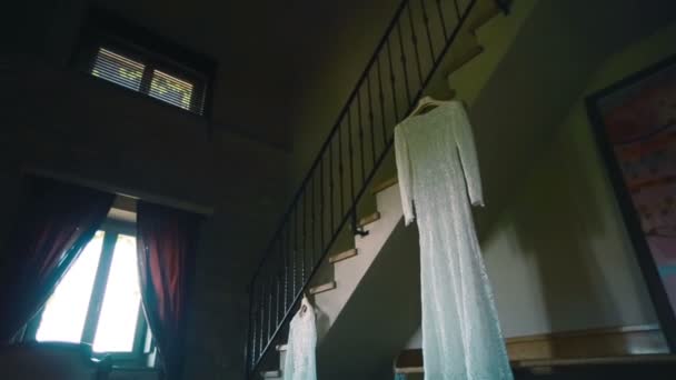 Vestido de noiva de renda pendurado na escada na sala de antiguidades. Panela — Vídeo de Stock