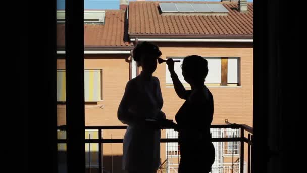 Maquillaje artista aplicar maquillaje hasta la novia. Silueta contra una casa roja — Vídeo de stock