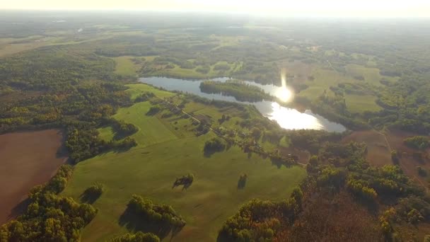 Vista aérea 4K - sobrevoando campos colhidos e lago no campo em clima ensolarado - cores do outono — Vídeo de Stock