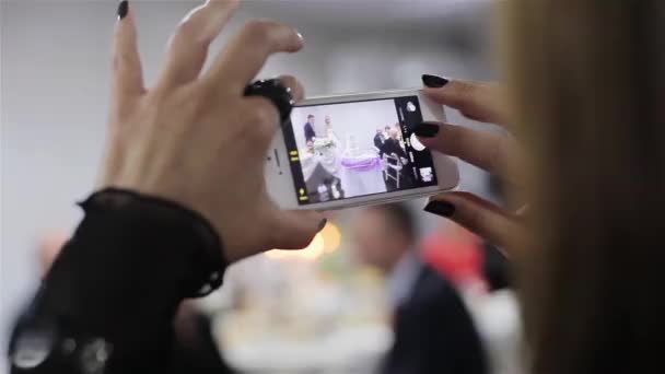 Una chica haciendo video de una pareja de boda cortando un pastel de bodas — Vídeos de Stock